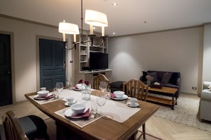 A dining area with a wooden table set for four, a television in the background, and a sofa in the living area. - Big Apt, Hidden Gem, Fully Equipped 2 big Br, 2 Ba, Spacious Living in Dt (Bangkok)