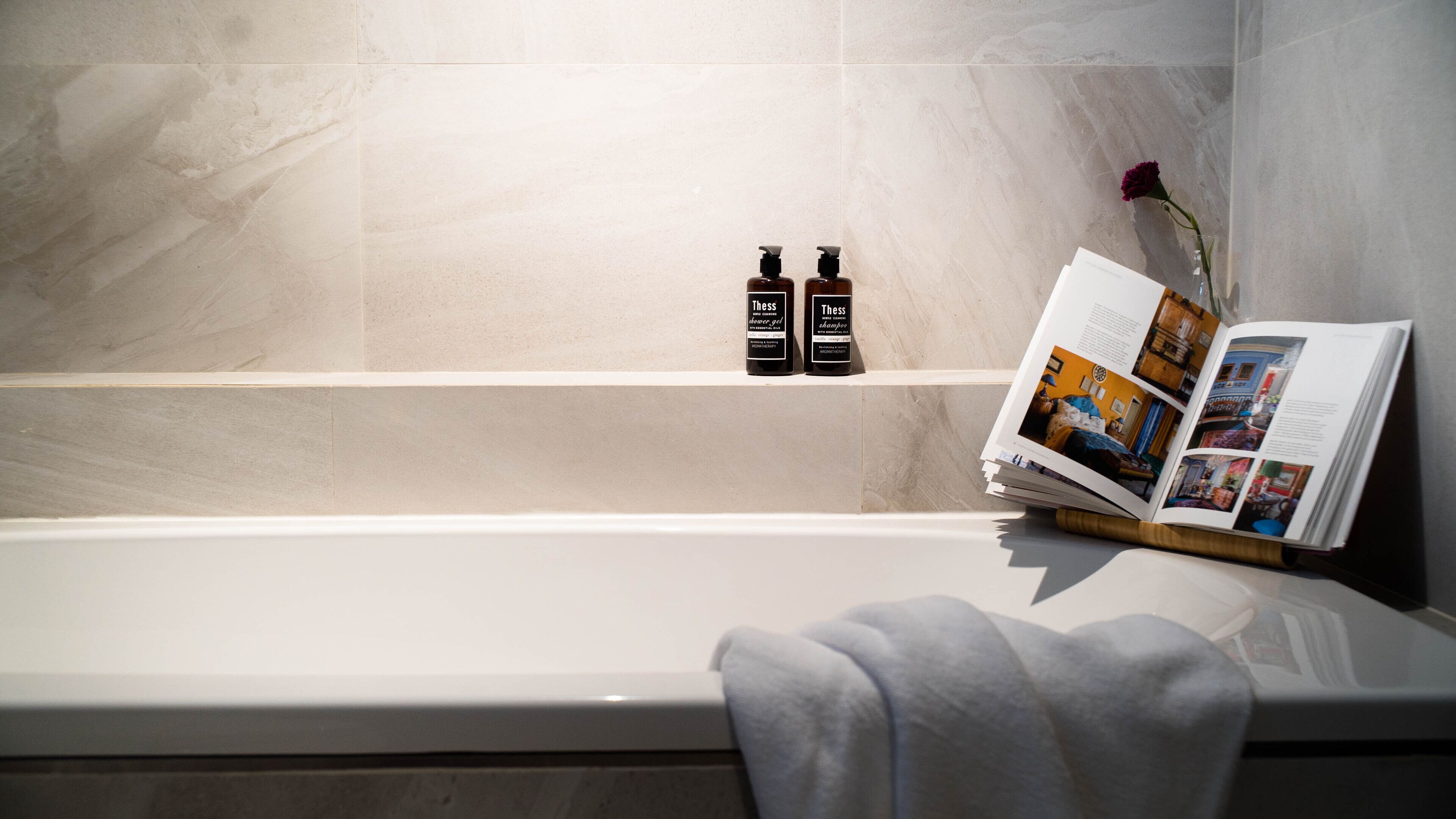 A bathroom with a bathtub, two bottles of shampoo, and a book on a side table.