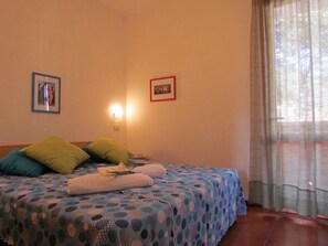 A bedroom with a bed, pillows, a wall-mounted light, and a window with curtains.