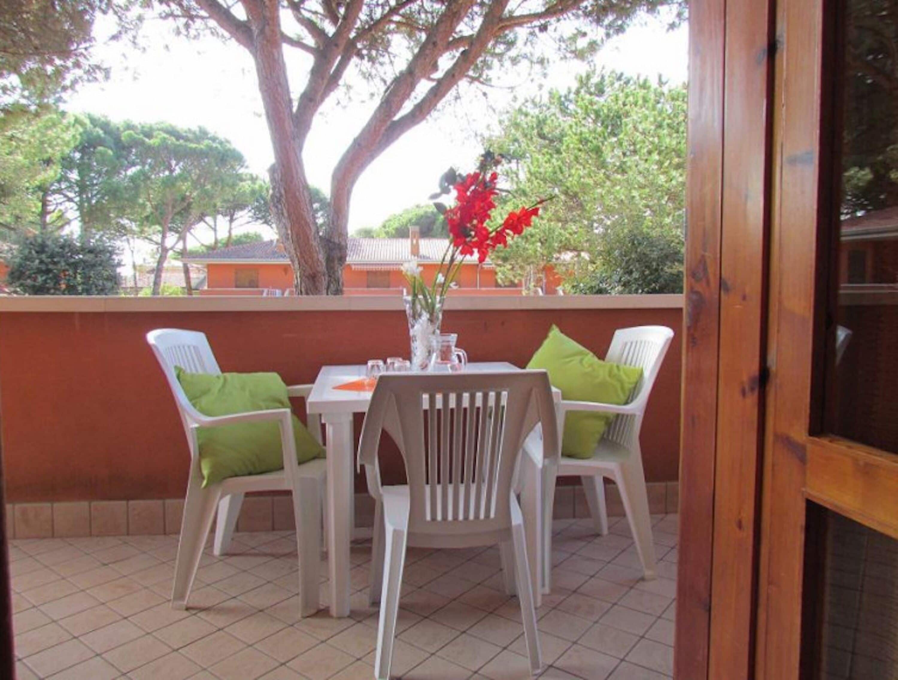 Eine Terrasse mit Tisch und Stühlen, eine Vase mit Blumen und ein großer Baum im Hintergrund.