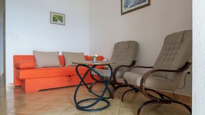 Een woonkamer met een bank, twee stoelen, een bijzettafeltje en een schilderij aan de muur.