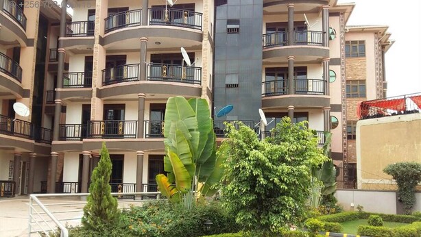 A multi-story residential building with balconies, satellite dishes, and a well-maintained garden with hedges and a central tree. - a Wonderful Fully Furnished Apartment in Kampala (Kampala)