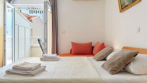Quarto com cama, almofadas, toalha dobrada, janela e um quadro na parede.