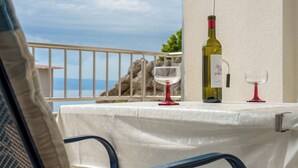 Uma mesa com uma garrafa de vinho e duas taças, numa varanda com vista para o mar.