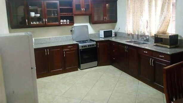A compact kitchen with dark wooden cabinets, a built-in microwave, a stove, and a refrigerator. - A Fully Furnished Apartment in the City of Kampala (Kampala)