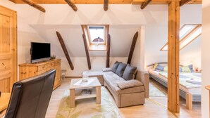 Ein Loft-Zimmer mit Holzbalkendecke, einer Couch, einem Fernseher und einem kleinen Fenster.