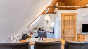 Ein Essbereich mit Holztisch, Stühlen, einer Pendelleuchte und einer Küche im Hintergrund.