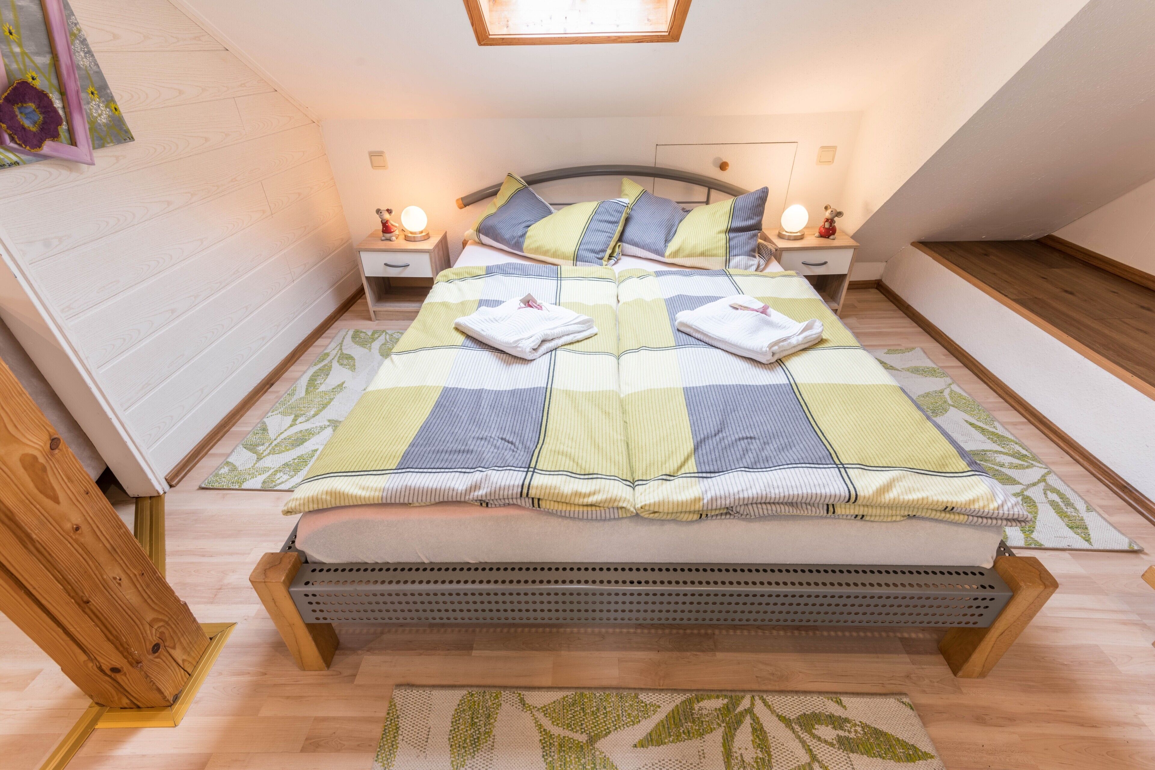 Une chambre  à coucher avec un lit, des tables de chevet, une commode, un plancher en bois et un plafond en pente.