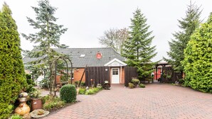 Ein mit Backsteinen gepflasterter Innenhof mit Holzlattenzaun, Blumentöpfen und einem Gebäude mit weißer Tür.