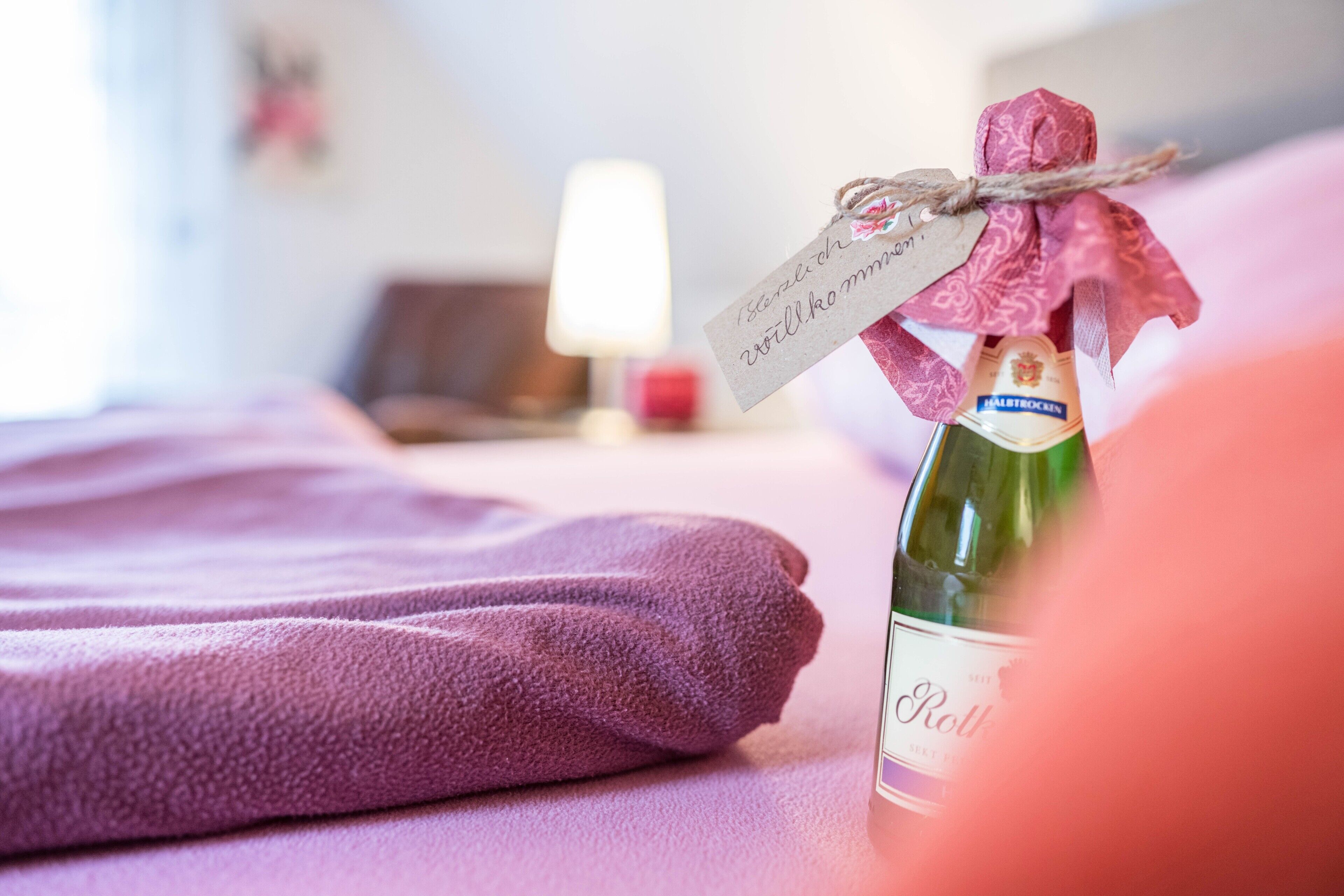 A bottle of wine with a tag, a purple towel, and a lamp in the background.