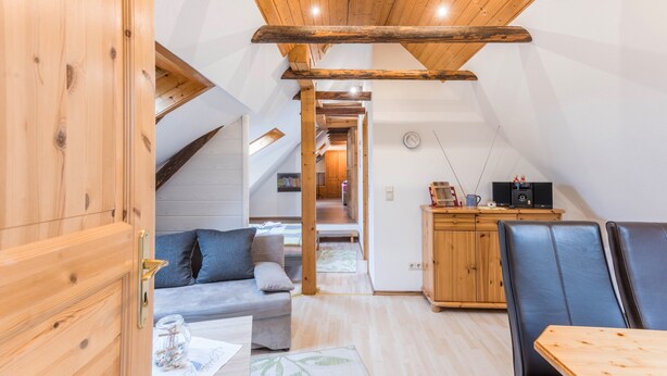 Ein gemütliches Zimmer mit Holzbalkendecke, einer Couch, einem Esstisch und einer Küchenzeile.