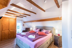 Un dormitorio con una cama grande, vigas de madera, un armario y una mesita de noche con lámpara.