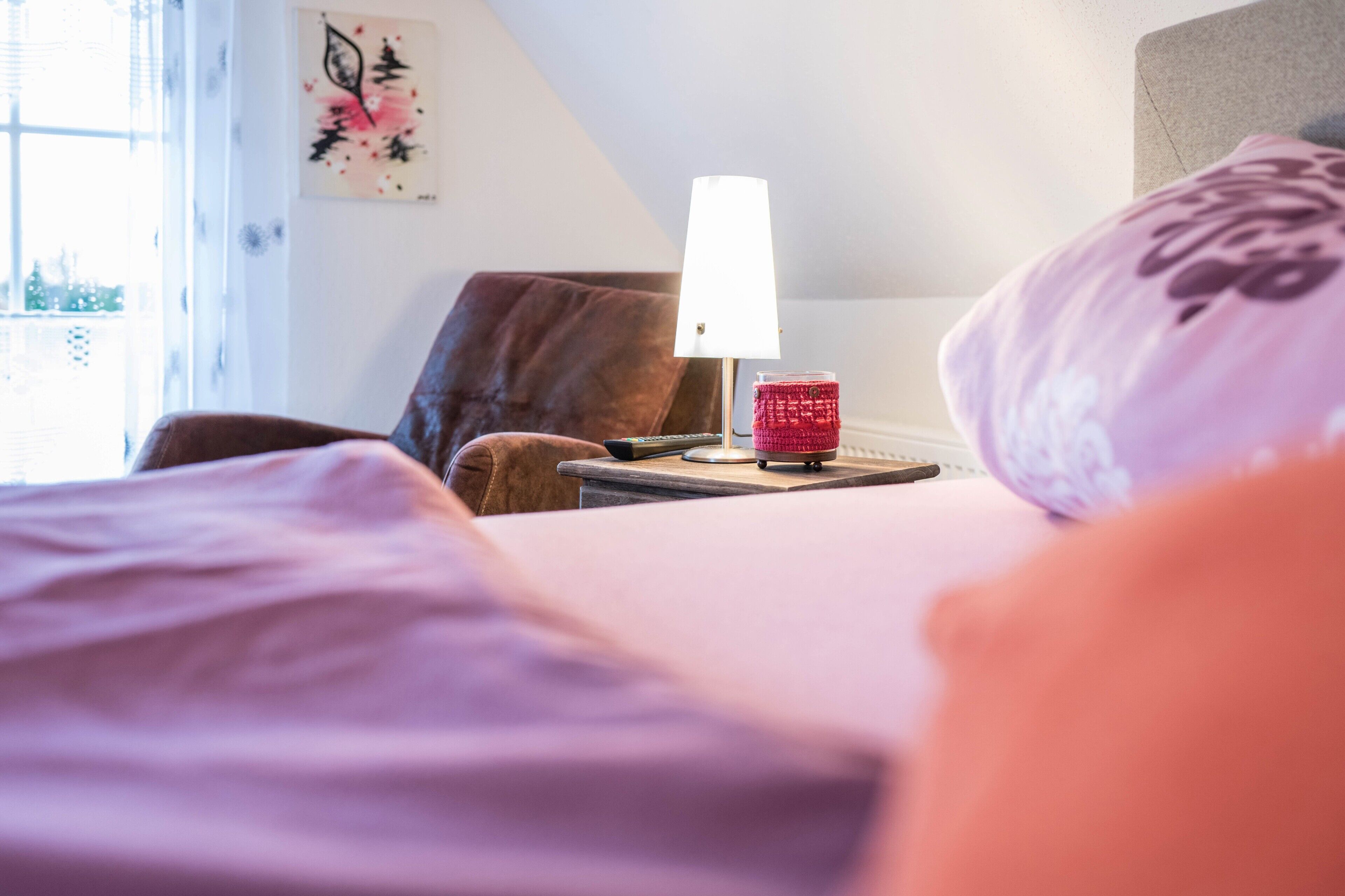 Een hotelkamer met een bed, een nachtkastje met een lamp, een afstandsbediening en een decoratief object op het nachtkastje.