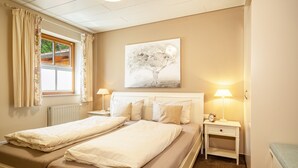 Una cama doble con cabecera, dos mesitas de noche con lámparas, una ventana con cortinas y un cuadro colgado en la pared.