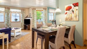 Un comedor con una mesa dispuesta para cuatro personas, un televisor y una ventana con cortinas.