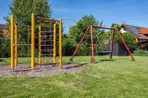 A playground with yellow and red play structures, surrounded by grass and trees.