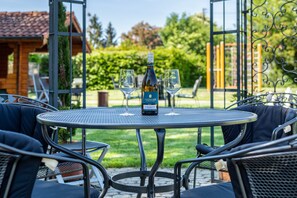 A round metal table with two wine glasses and a bottle of wine, surrounded by dark cushioned chairs, set outdoors with a view of a garden and a building in the background. - Beautiful Vacation Apartment 4 on "Trostelhof" with Balcony (Salem-Neufrach)