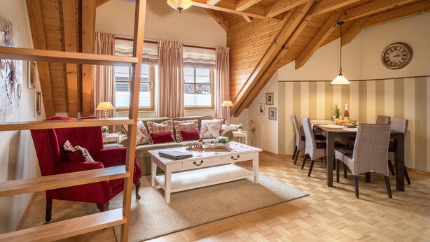 A cozy living room with a wooden ceiling, a white coffee table, a red armchair, and a dining area with a table and chairs.
