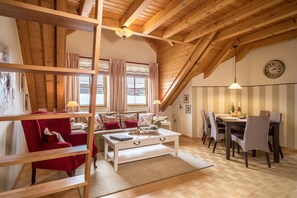 Ein gemütliches Wohnzimmer mit Holzboden, einem weißen Couchtisch, einem roten Sessel und einem Essbereich mit Tisch und Stühlen.