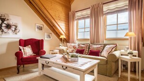 A cozy living room with a red armchair, a sofa, a coffee table, and a window with curtains.