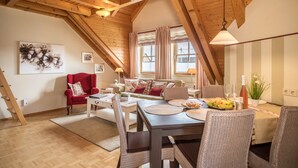 A cozy loft-style room with a dining table, chairs, a red armchair, and a staircase.