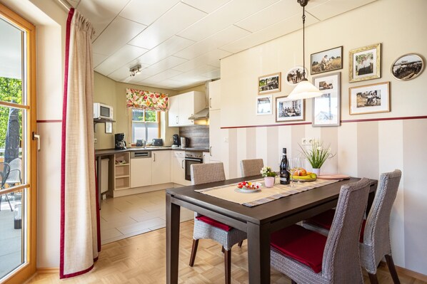 Uma sala de jantar com mesa, cadeiras e cozinha ao fundo.