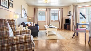 Un salón con sofá, sillón, mesa de centro, televisor y vistas al exterior.