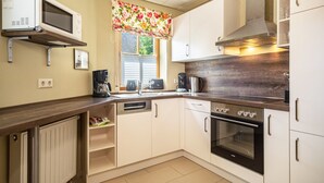 Una cocina con armarios blancos, microondas, estufa, lavavajillas y una ventana con un adorno floral.