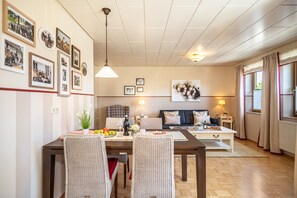 Un coin repas avec une table en bois, des chaises en osier et un canapé en arrière-plan.