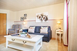 En stue med sofa, lænestol, sofabord og to sengeborde med lamper.