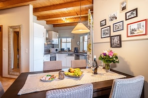 A dining area with a wooden table, chairs, a vase of flowers, and a fruit bowl.