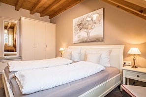 A bedroom with a double bed, a wardrobe, a bedside table with a lamp, and a painting on the wall.