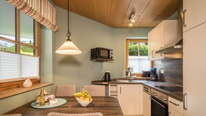 Cocina compacta con microondas, cafetera y horno. Hay una mesa de comedor con sillas de mimbre y un bol de fruta.