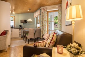 Un salon confortable avec un canapé, une table à manger et des chaises, un coin cuisine équipé d’un four à micro-ondes, et une fenêtre avec des rideaux.