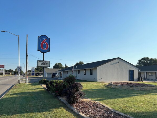 A motel with a large '6' sign, a speed limit sign, and a sign indicating upcoming amenities.