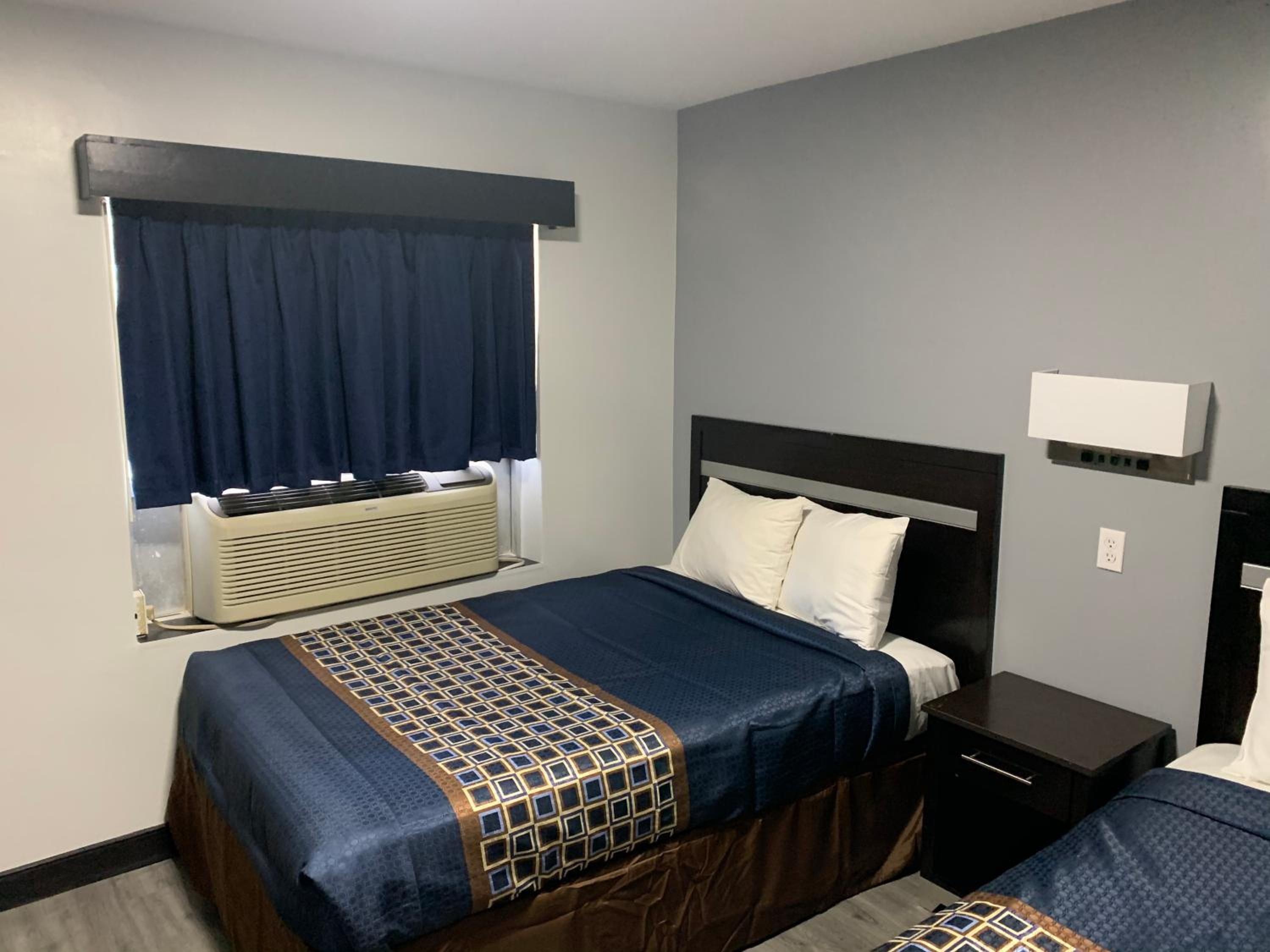 A hotel room with a bed, bedside table, and a window with curtains.