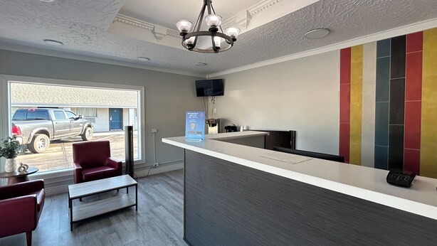 A reception area with a counter, seating, a television, and a view of a parked truck outside. - Motel 6 Ponca City, OK (Ponca City)