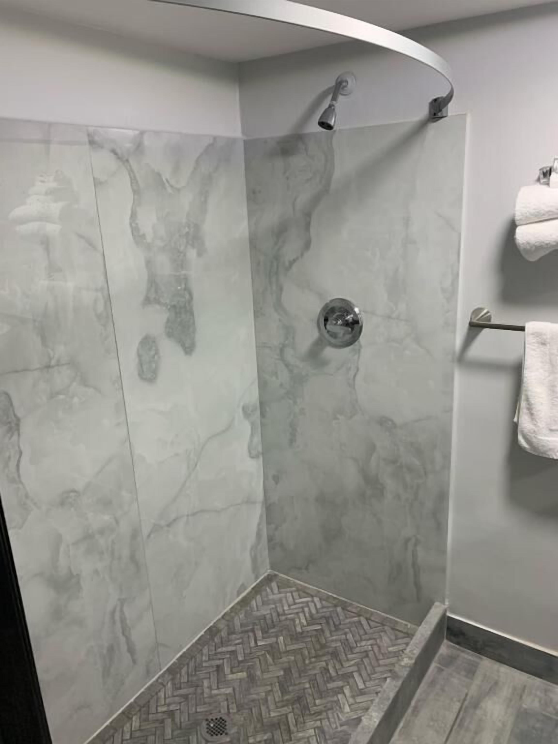 A shower area with a herringbone-patterned floor, a showerhead, and a towel rack with towels.