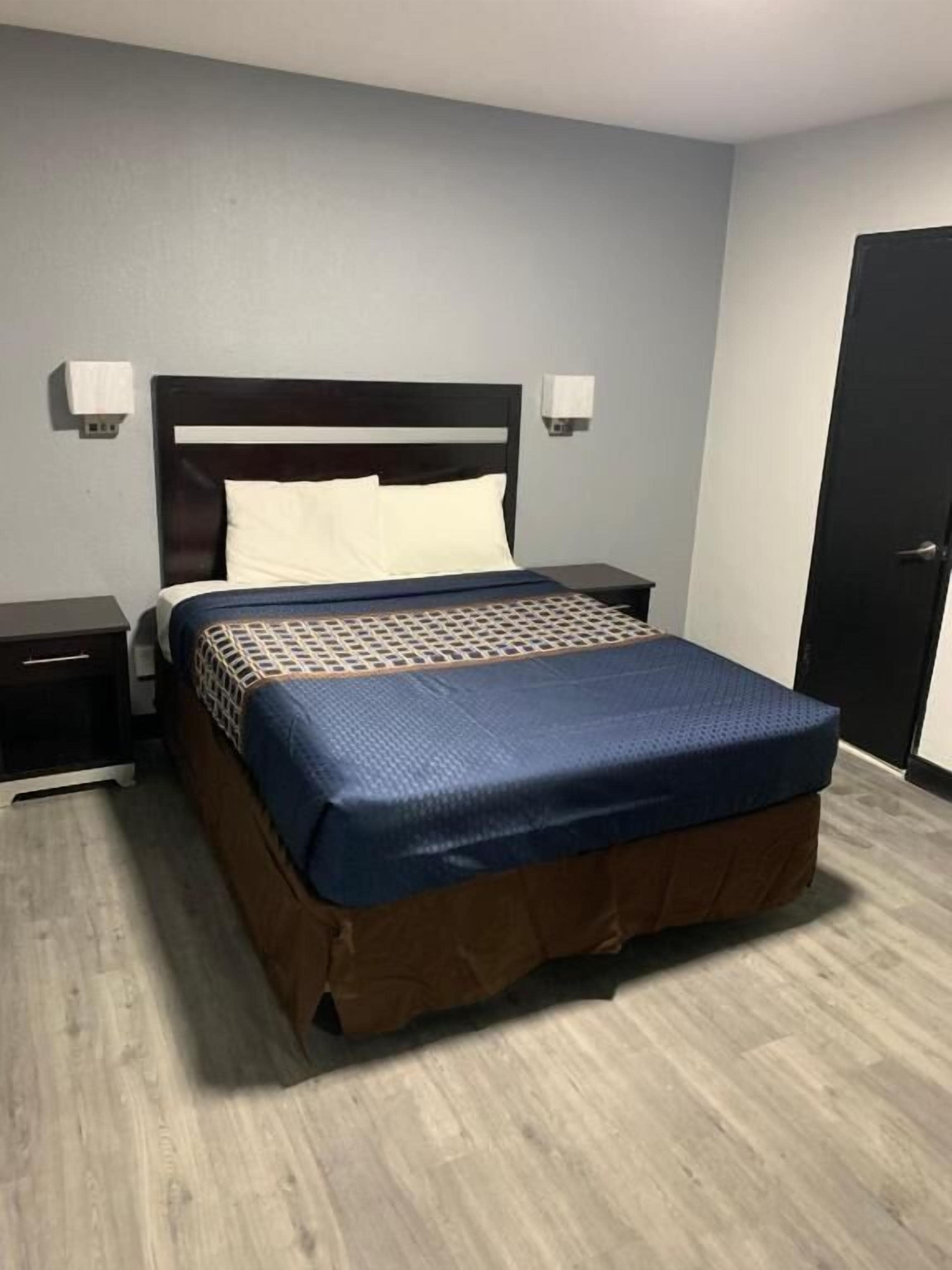 Habitación estándar de hotel con una cama individual, una mesita de noche, una lámpara de pared y una puerta.