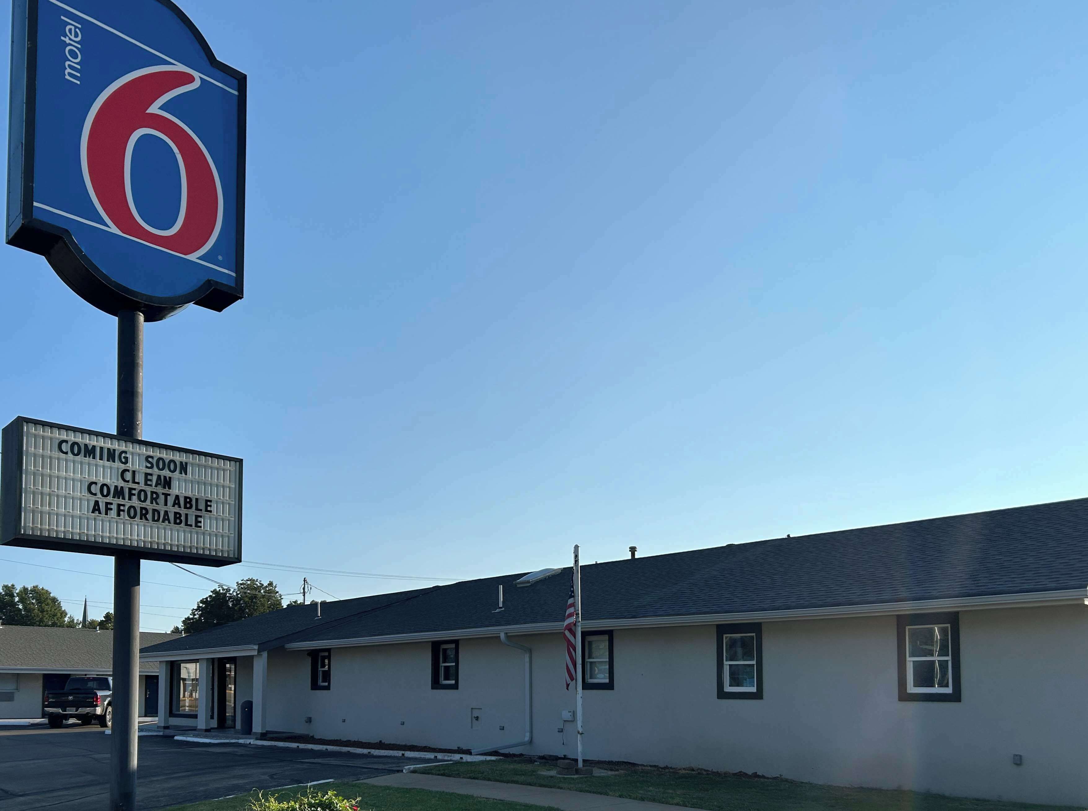 Segnale di motel con logo '6' e cartello che indica 'PROSSimamente: pulito, confortevole, conveniente'.