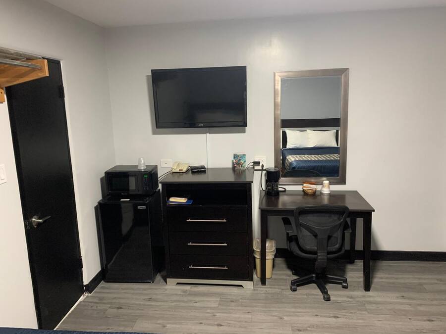 A hotel room with a desk, a chair, a television, a bed with a headboard, and a door.