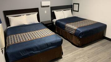 A hotel room with two beds, each with a headboard, a nightstand, a wall-mounted light, and a framed picture.