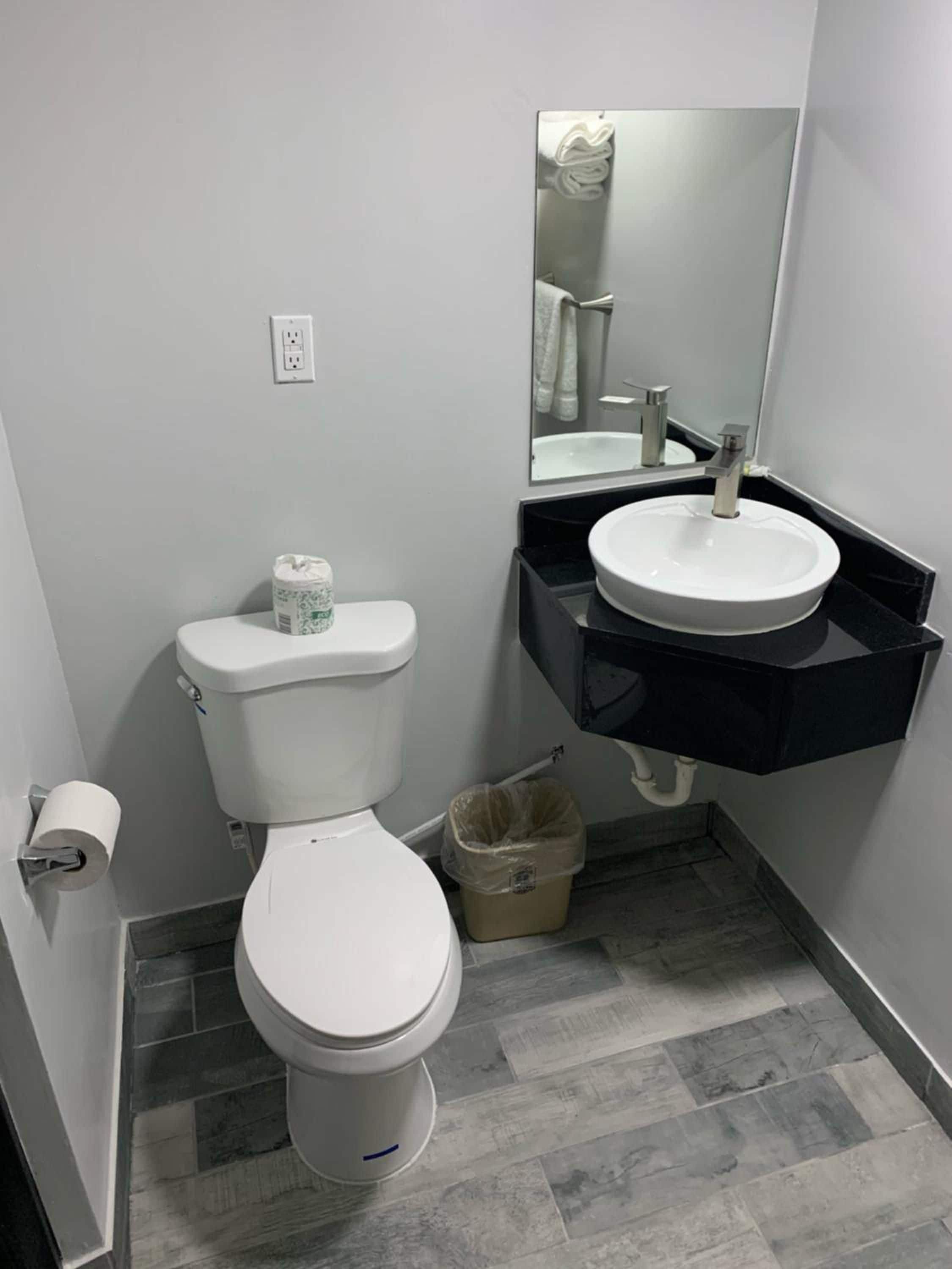 Un baño con inodoro, lavamanos, espejo y un bote de basura.