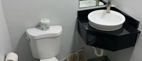 Un baño con inodoro, lavamanos, espejo y un bote de basura.