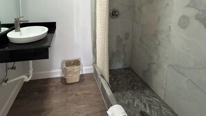 A bathroom with a white sink, black countertop, and a shower with a textured wall. - Motel 6 Ponca City, OK (Ponca City)