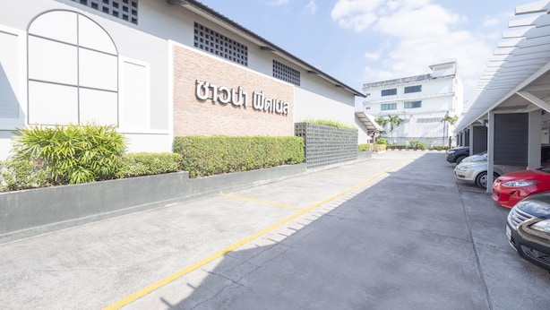A building with a sign in a foreign language, a parking lot with cars, and a clear sky. - OYO 75382 Chonburi Hotel (Chonburi)