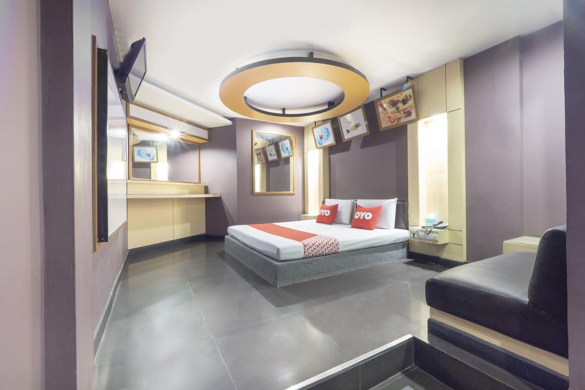 A modern hotel room with a bed, a desk, a chair, a mirror, and artwork on the walls.