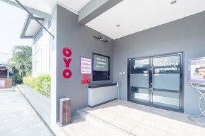 A hotel entrance with a reception desk, a digital screen, and a signboard with operating hours.
