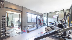 A modern gym with various exercise equipment, a mirrored wall, and large windows. - OYO 75382 Chonburi Hotel (Chonburi)