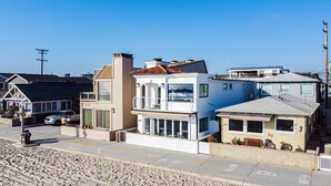 A coastal residential area with modern houses, including a two-story house with a large balcony and a view of the ocean. - Entire Boardwalk Home on the Beach in Newport Beach with Beautiful Views (Newport Beach)